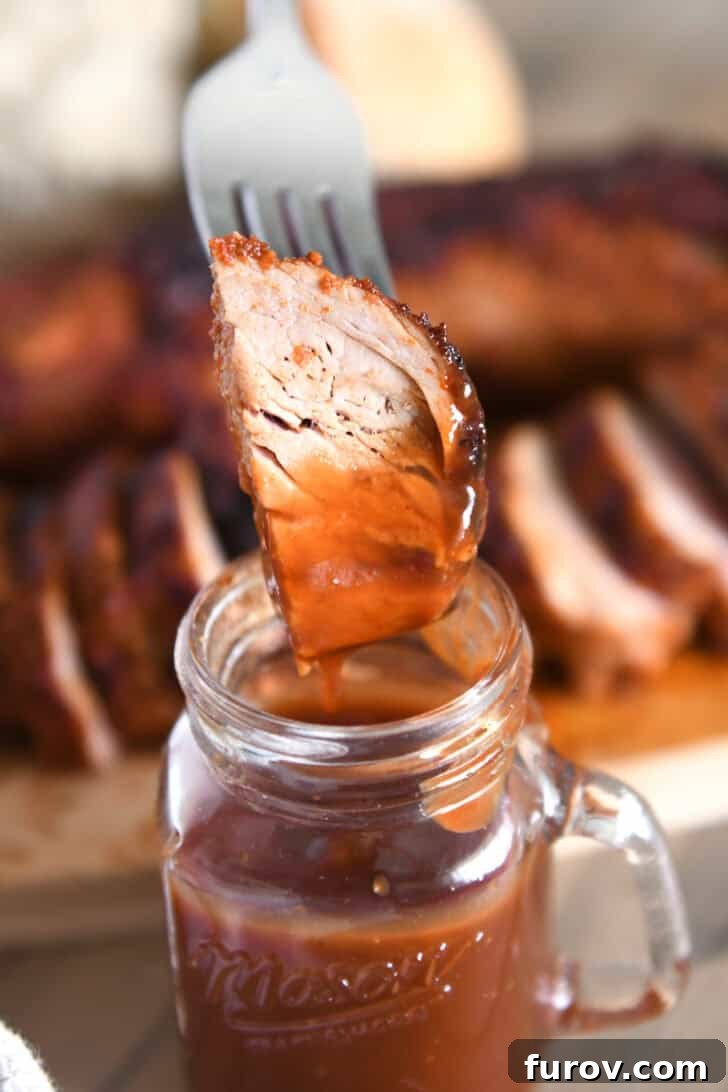 Speedy and Succulent Air Fryer Pork Tenderloin 8 A fork piercing a piece of perfectly cooked pork tenderloin, ready to be dipped into BBQ sauce.