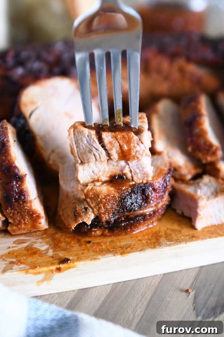 Speedy and Succulent Air Fryer Pork Tenderloin 9 A fork lifting two stacked slices of succulent pork tenderloin from a wooden cutting board, ready to be enjoyed.