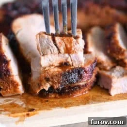 Speedy and Succulent Air Fryer Pork Tenderloin 10 Fork piercing stack of two pieces of cooked pork tenderloin on wood cutting board.