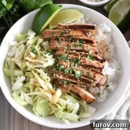 Top down photo of white bowl with chopped cabbage, white rice, grilled chicken, lime wedges, chopped cilantro and toasted sesame seeds.