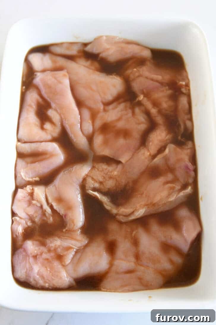 White pan with thinly sliced chicken breasts and Asian-style marinade.