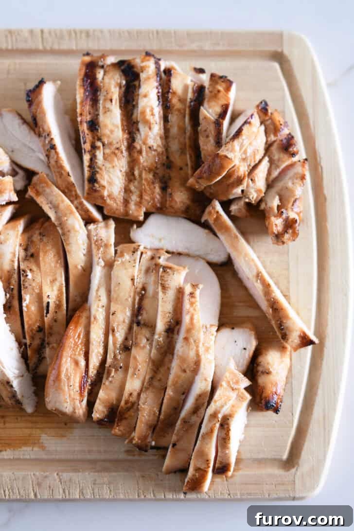 Thinly sliced grilled chicken on wood cutting board.