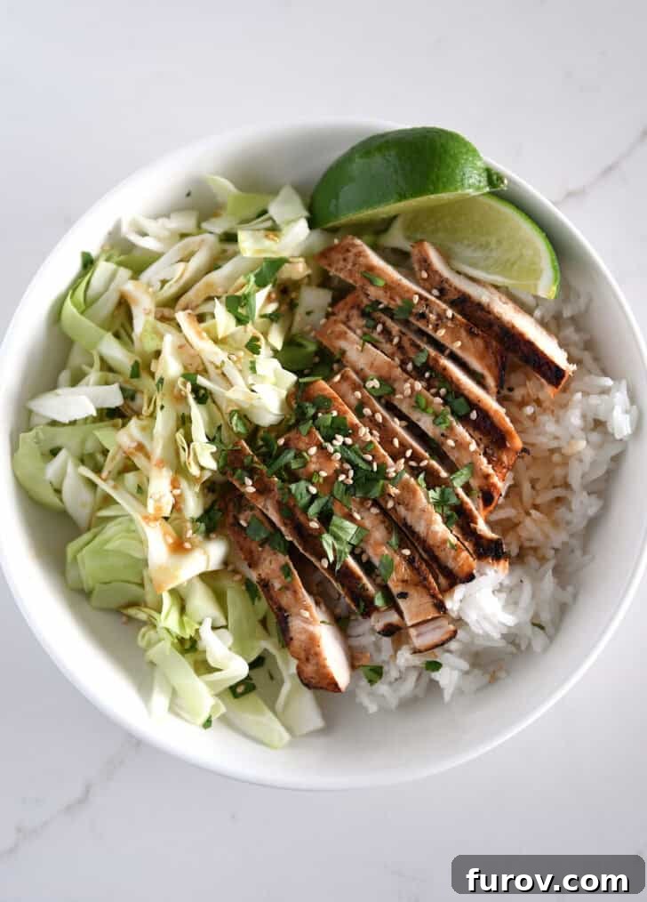 White bowl with chopped cabbage, white rice, grilled chicken, cilantro and lime wedges.
