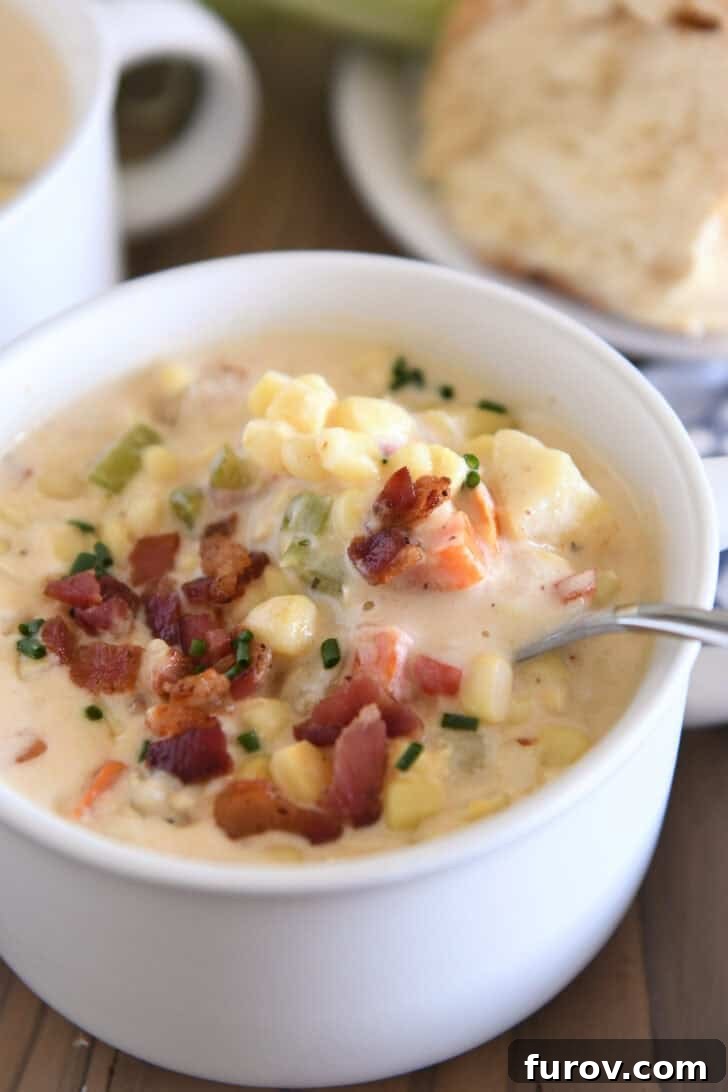 A beautifully presented white bowl of creamy summer corn chowder, garnished with fresh corn kernels, crispy bacon bits, tender potatoes, and vibrant carrots. A spoon rests in the bowl, ready to scoop up the deliciousness.