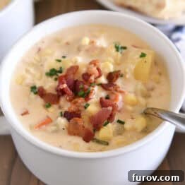 White bowl with spoon scooping up chowder with fresh corn, bacon, potatoes and carrots.