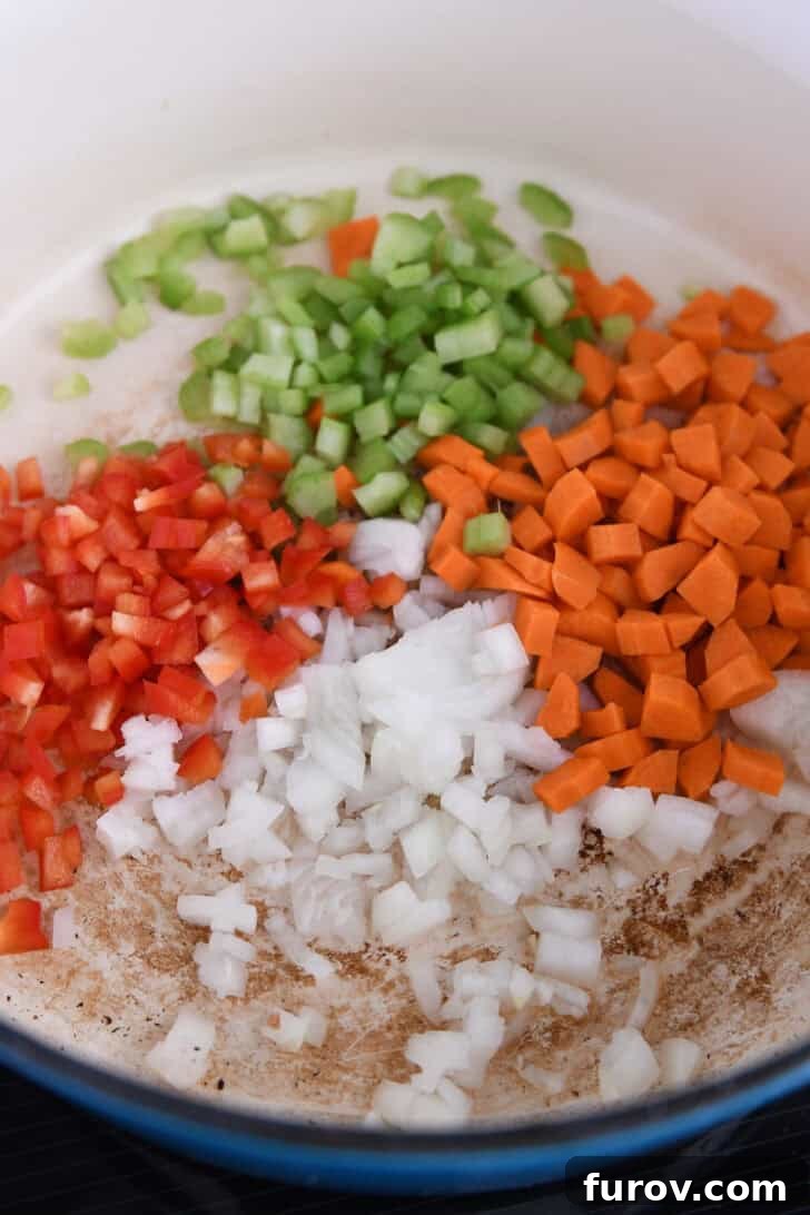 A Dutch oven pot filled with a colorful medley of red bell peppers, celery, carrots, and onions, ready to be sautéed for a rich chowder base.