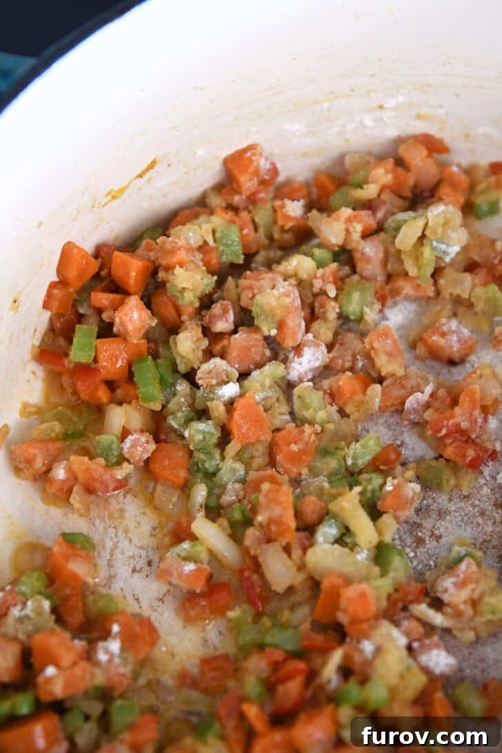 Close-up view of sautéed carrots, celery, onions, and bell peppers, stirred together with flour to create a roux, thickening the soup.