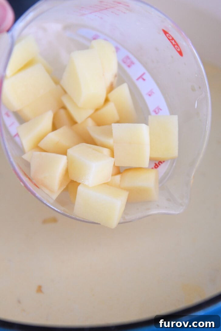 Diced Yukon gold potatoes being added to a bubbling pot of corn chowder, ready to simmer until tender.