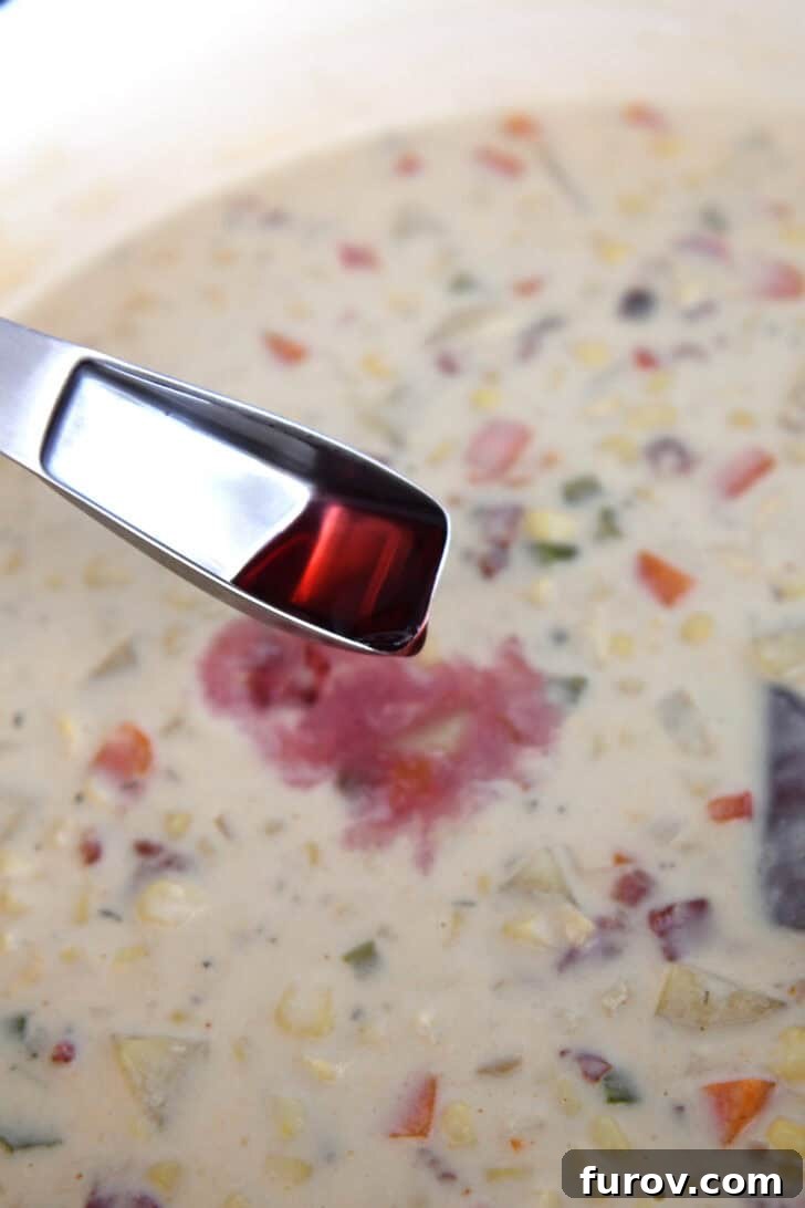 A tablespoon of red wine vinegar being carefully poured into a simmering pot of creamy corn chowder, adding a vital touch of balance.