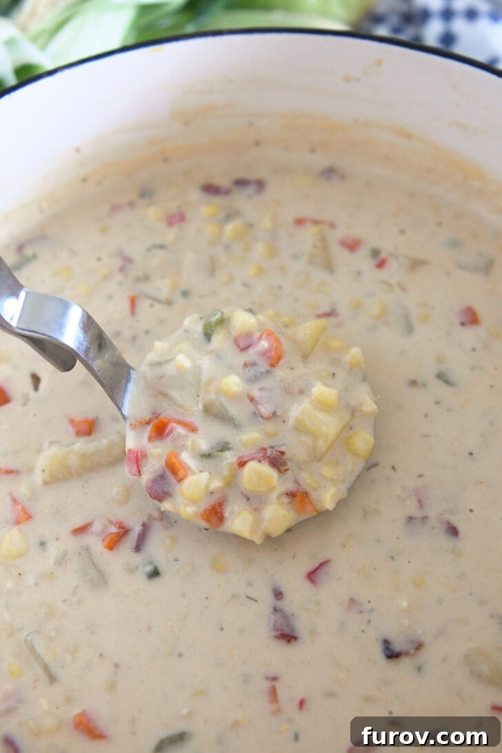 A ladle expertly scooping up a generous portion of thick and creamy corn chowder, revealing tender carrots, savory bacon, and potatoes.