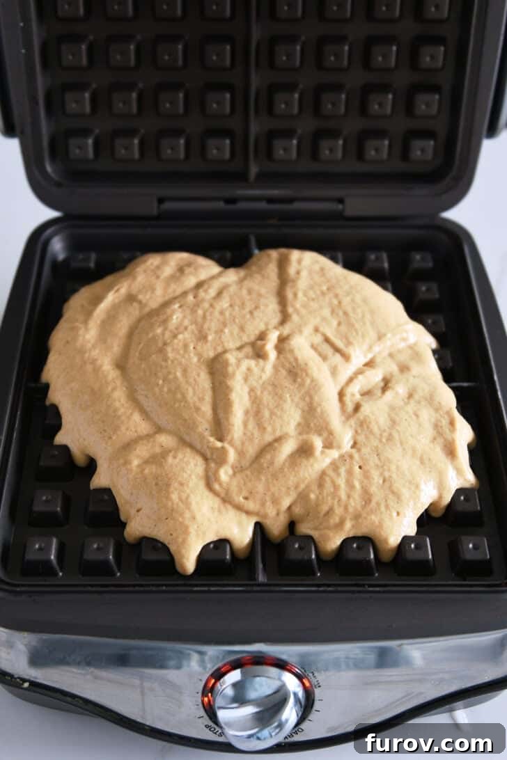 Pumpkin waffle batter spread evenly in a square waffle iron, just before cooking.
