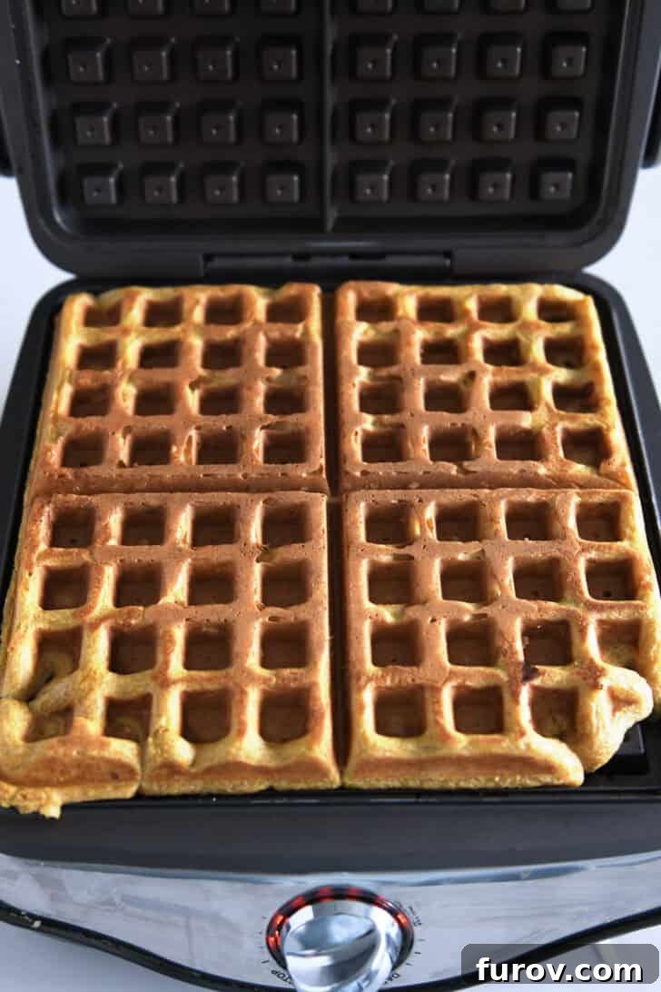 Perfectly baked pumpkin waffle with the lid open on a waffle maker, revealing its golden-brown texture.
