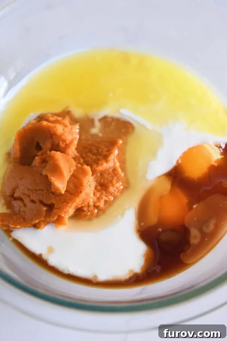 Glass bowl containing canned pumpkin puree, fresh eggs, creamy buttermilk, melted butter, and a hint of vanilla extract, ready to be combined.
