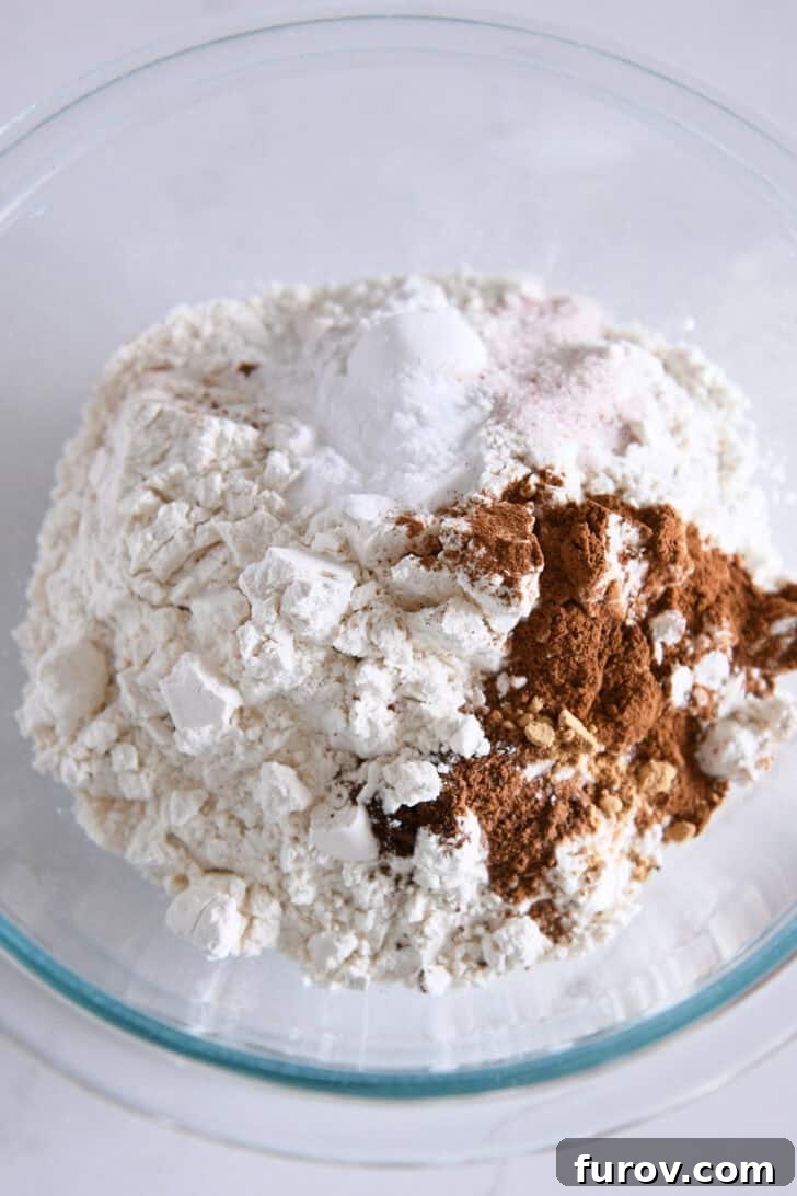 Glass bowl filled with all-purpose flour, ground cinnamon, nutmeg, baking powder, baking soda, and salt – the perfectly measured dry ingredients.