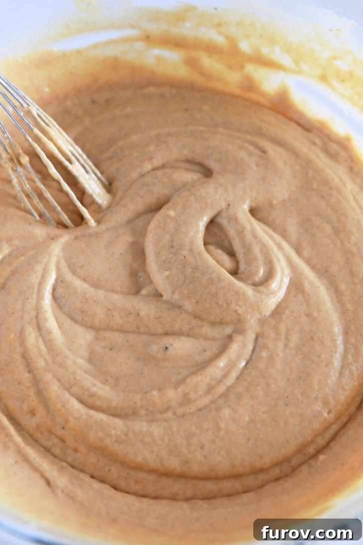 Smooth and perfectly mixed pumpkin waffle batter in a glass bowl, with a whisk resting in it, ready for the waffle iron.