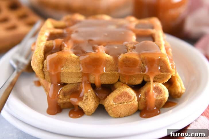 Two squares of fluffy pumpkin waffles on a white plate, generously smothered in homemade buttermilk caramel syrup and ready to be enjoyed.