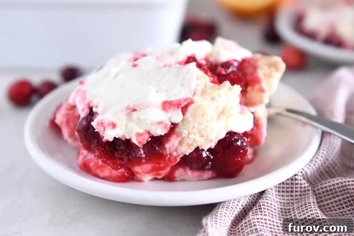 Scoop of cranberry orange layered angel food cake dessert on white plate with spoon, highlighting the distinct and inviting layers.
