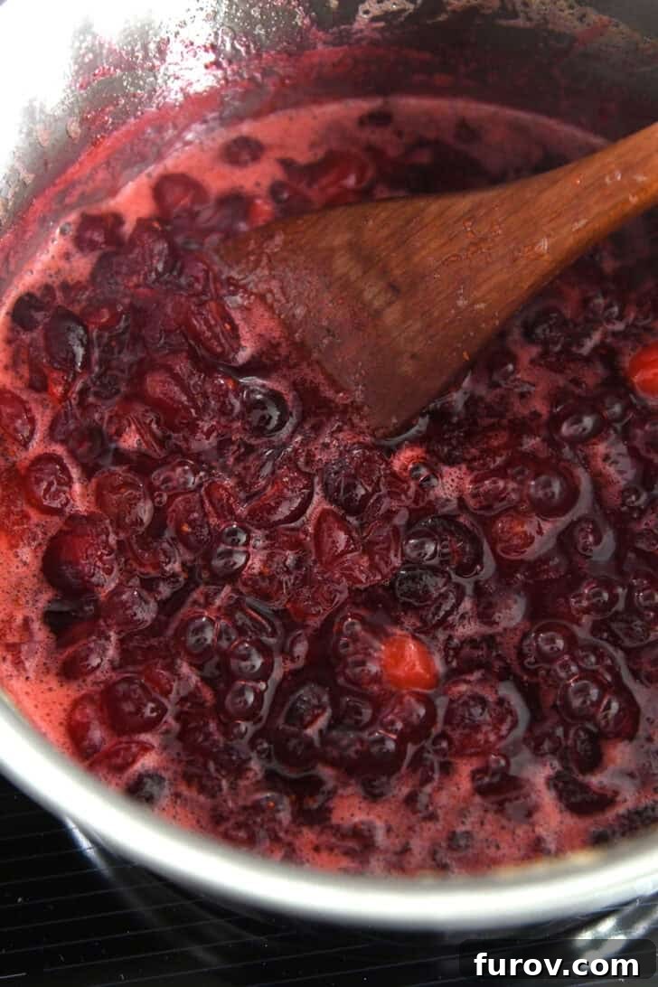 Saucepan with thick, simmered mixture of fresh cranberries, orange juice and sugar, showing the rich color and texture.