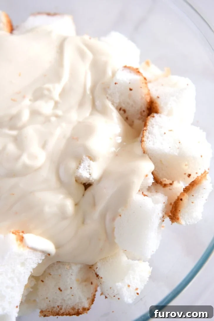 Glass bowl showcasing angel food cake cubes thoroughly coated with the creamy mixture.