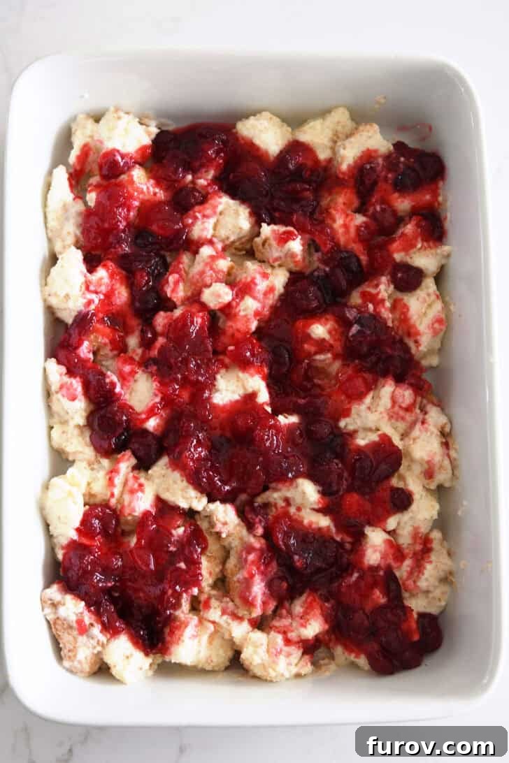 White baking dish with the first layer of cream-covered angel food cake cubes topped with the vibrant cranberry orange mixture.