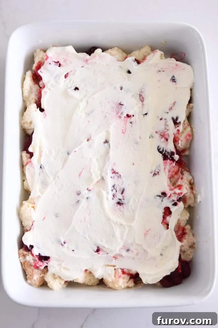 White baking dish showcasing a smooth layer of whipped cream spread over the cranberry orange and angel food cake layers.