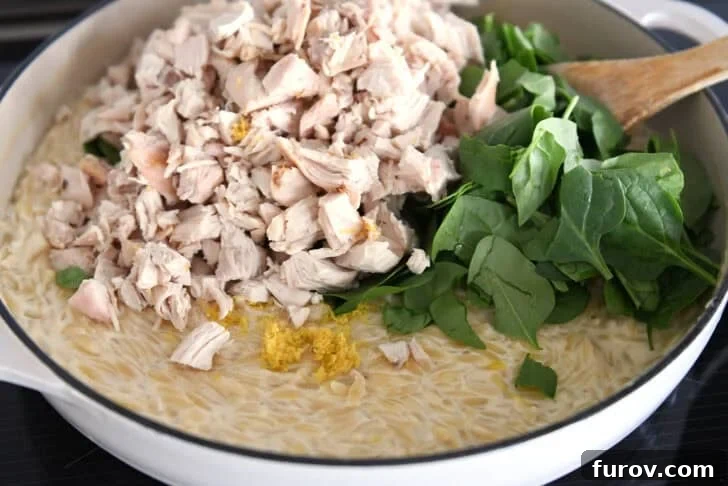 Chopped chicken, lemon zest and fresh spinach in white pan with creamy orzo.