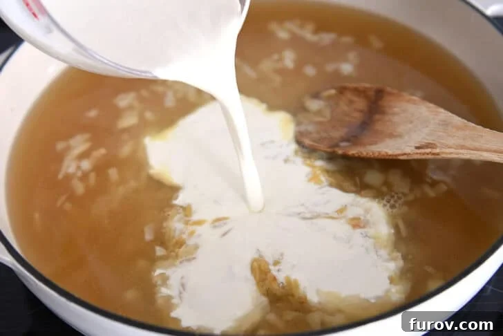 Pouring cream into white pan with broth and orzo.