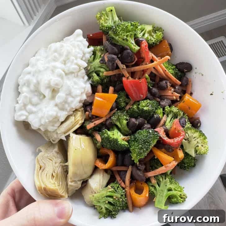 White bowl with broccoli, peppers, carrots, black beans, artichokes, and cottage cheese.