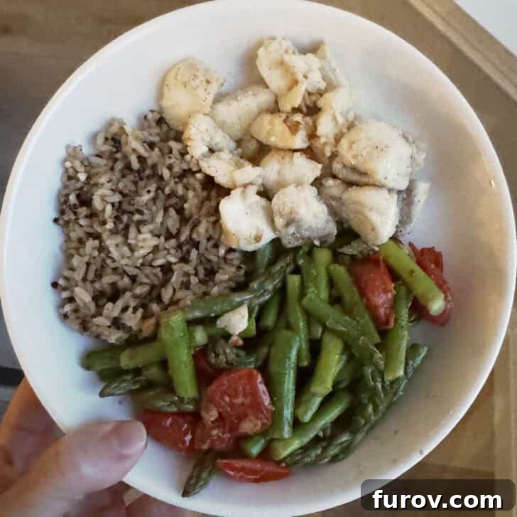 White bowl with brown rice, cod, tomatoes, and asparagus.