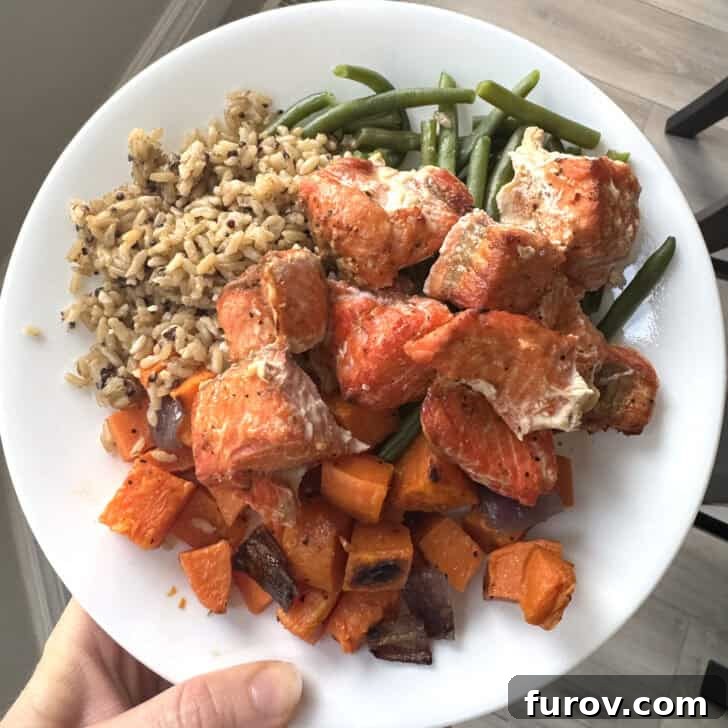 White plate with brown rice, sweet potatoes, green beans and salmon bites.