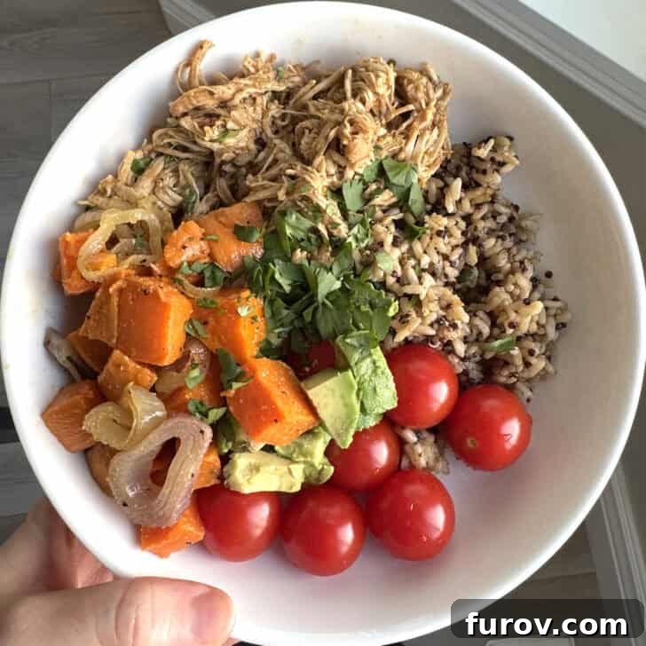 White plate with sweet potatoes, onions, avocados, cherry tomatoes, brown rice and salsa verde chicken.