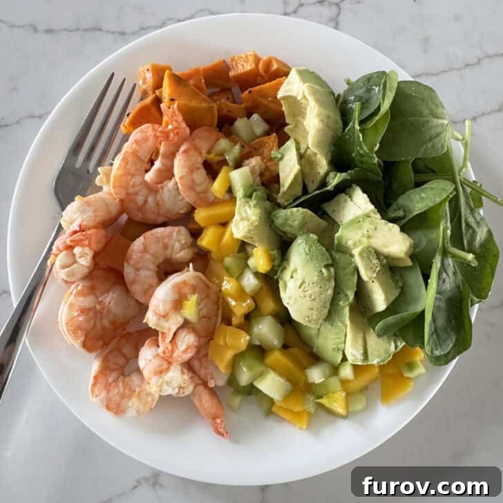 White plate with shrimp, mango, cucumbers, spinach, avocado and sweet potatoes.