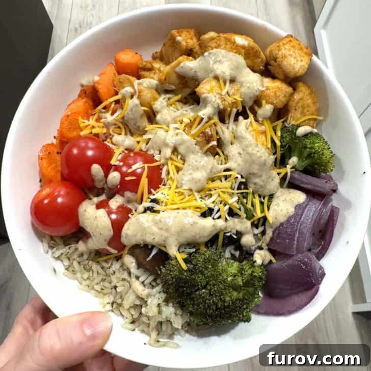 White bowl with cilantro lime rice, broccoli, onions, cherry tomatoes, carrots, chicken, cheese and Bitchin' sauce.