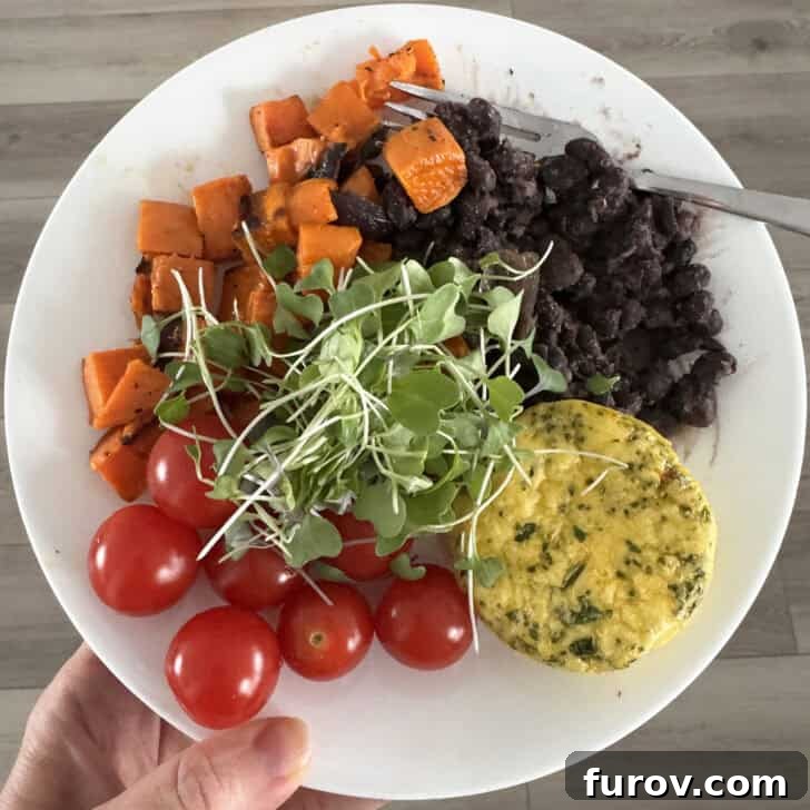 White plate with egg bite, black beans, sweet potatoes, cherry tomatoes and microgreens.