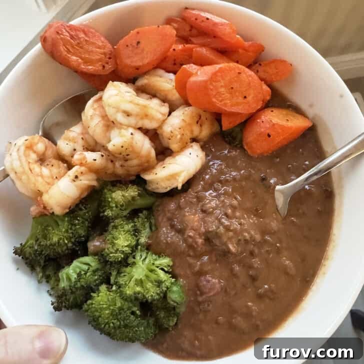 White bowl with lentil soup, broccoli, shrimp and carrots.