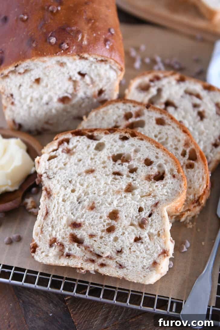 A perfectly golden slice of homemade Cinnamon Burst Bread resting on brown parchment paper, with a small wooden dish of softened butter beside it, ready to be spread.