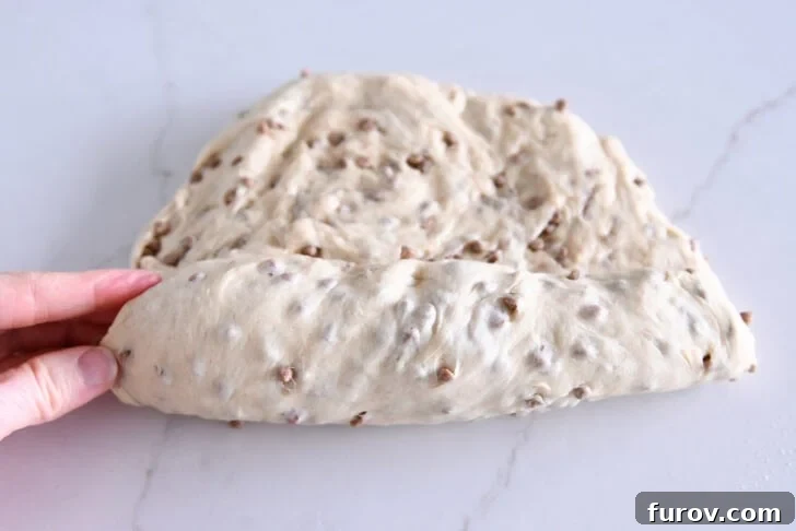 Hands demonstrating the rolling technique for Cinnamon Burst Bread dough, shaping it into a tight log before placement in a loaf pan.