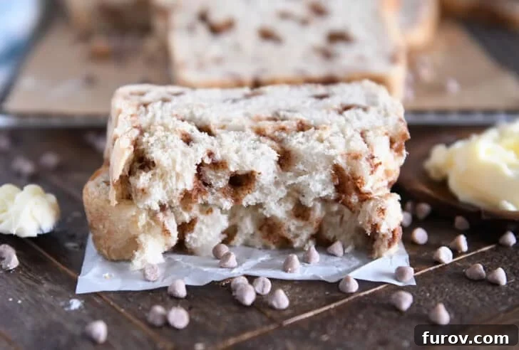 Two halves of a freshly baked loaf of Cinnamon Burst Bread, stacked invitingly on white parchment paper, revealing its moist, cinnamon-swirled interior.