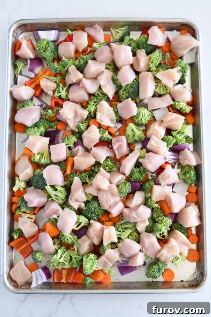 Sheet pan with red onions, carrots, bell peppers, chicken, and broccoli.