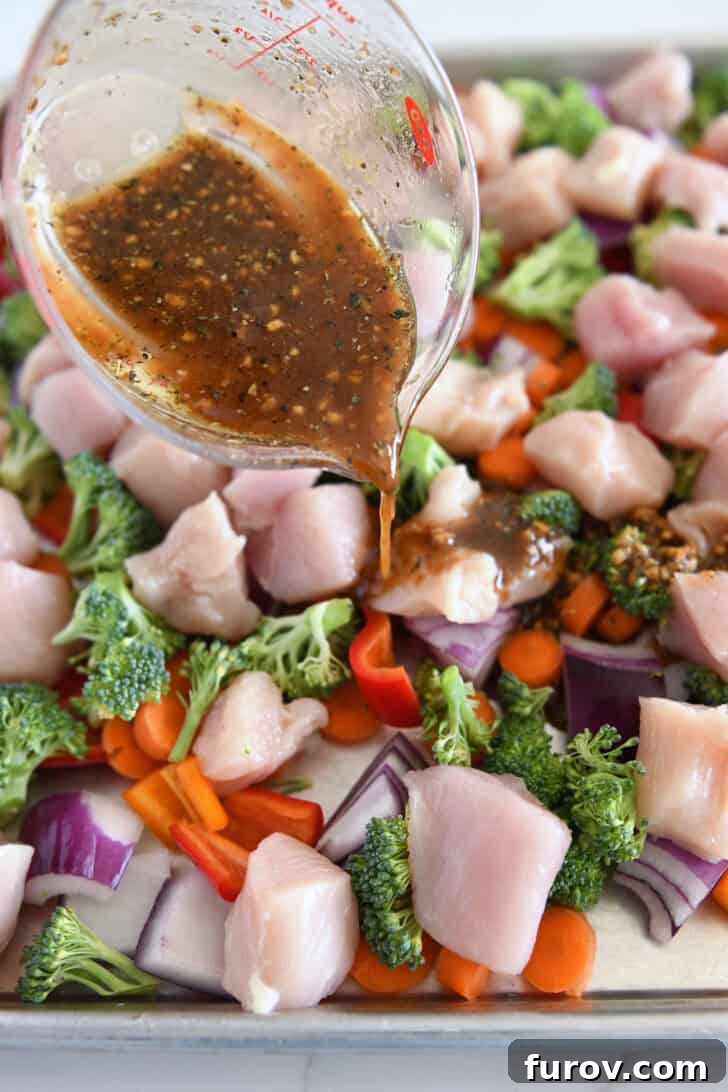 Pouring honey garlic sauce over chicken, broccoli, bell peppers, and carrots on sheet pan.