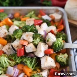 Serving spoon with cooked chicken, broccoli, carrots, bell peppers, and red onions.