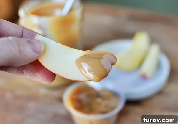 Whip Up Your Own Dulce de Leche 3 A hand holding a slice of crisp green apple, generously dipped into a rich, golden homemade dulce de leche, ready for a delicious bite.