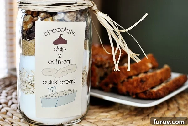 Homemade Oatmeal Chocolate Chip Jar Quick Bread 3 Layered dry ingredients in a mason jar for oatmeal chocolate chip quick bread, with a freshly baked and sliced loaf on a platter in the background.