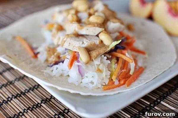 White tortilla topped with cooked rice, Asian chicken, veggies, and peanuts stacked on top.