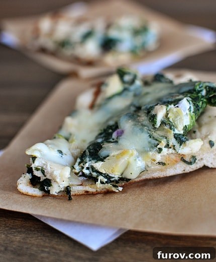 Luscious Spinach Artichoke Pizza 2 A slice of spinach artichoke pizza on a piece of parchment paper.