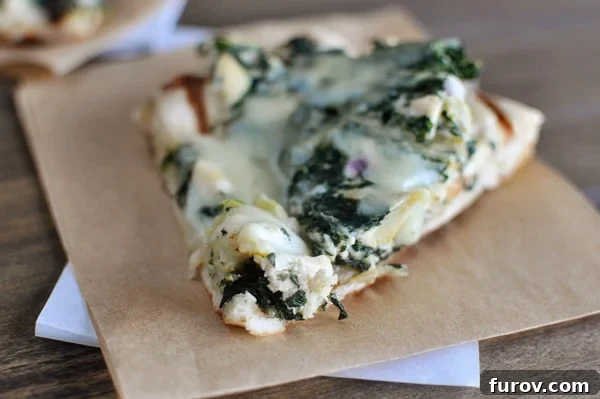 Luscious Spinach Artichoke Pizza 3 A slice of spinach artichoke pizza on a piece of brown parchment paper.