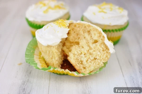 A perfectly baked lemon cupcake, expertly split in half to showcase its incredibly moist and tender crumb texture, resting on a paper muffin liner.