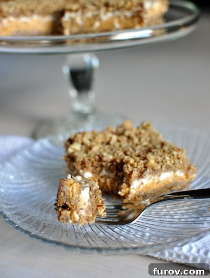 Autumn Pumpkin Cheesecake Streusel Bars 2 A glass plate with a pumpkin cheesecake crumble bar on it and a fork taking a bite out.