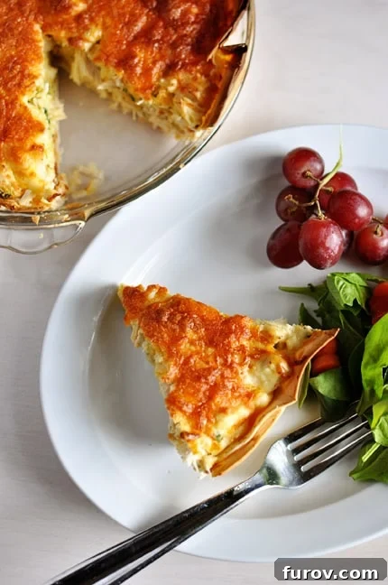 Hearty Chicken Quesadilla Casserole 2 A perfectly golden slice of cheesy chicken quesadilla pie on a white plate, served alongside a vibrant cluster of red grapes and a fresh green salad.