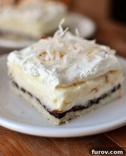 Dreamy Chocolate Coconut Cream Bars 3 A perfectly square slice of Chocolate and Coconut Cream Pie Bar, showcasing the distinct layers of crust, chocolate ganache, coconut cream, and a dollop of whipped cream garnished with toasted coconut.